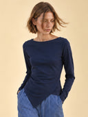 CELESTE-Shirt-tailliert-und-asymmetrisch-in-Deep-Blue, Oberkörper einer Frau mit dunkelblauem asymmetrischemLongsleeve und Hände in den Taschen mit Blick zur Seite.